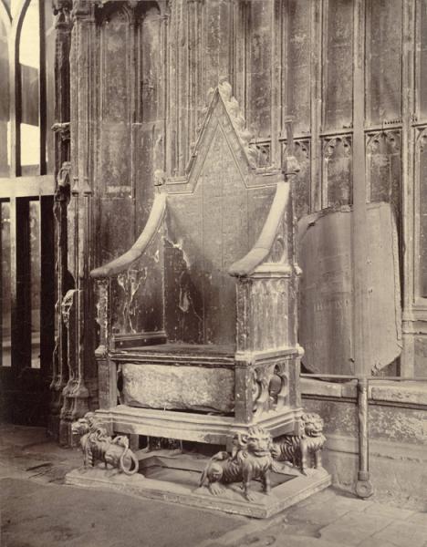 A sepia photo of a large throne with a stone block positioned in a cavity under the seat, in front of a wall of carved wooden panelling